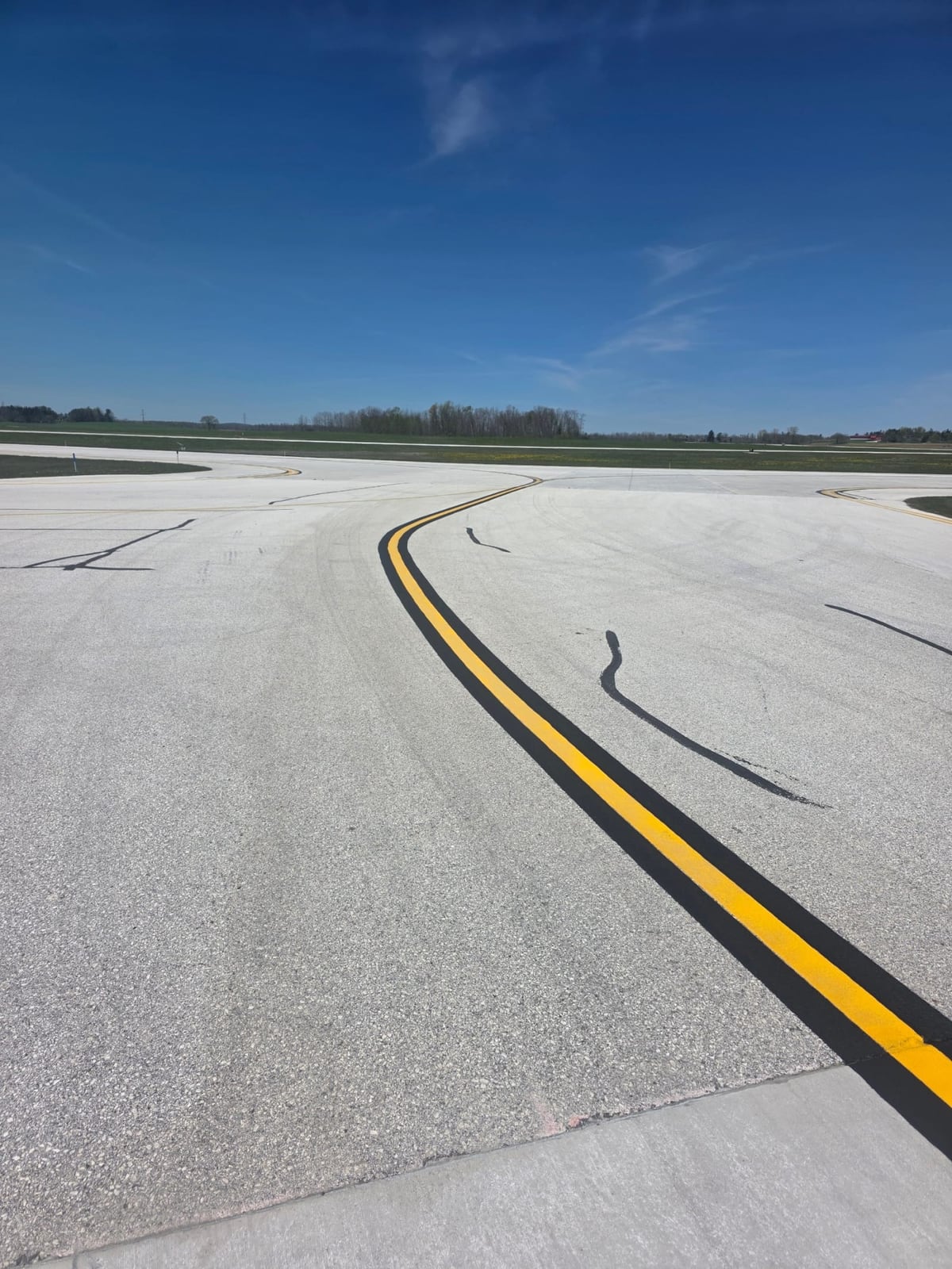 a curved double-yellow centerline freshly striped across a wide airfield surface by Draki Enterprises in Wisconsin