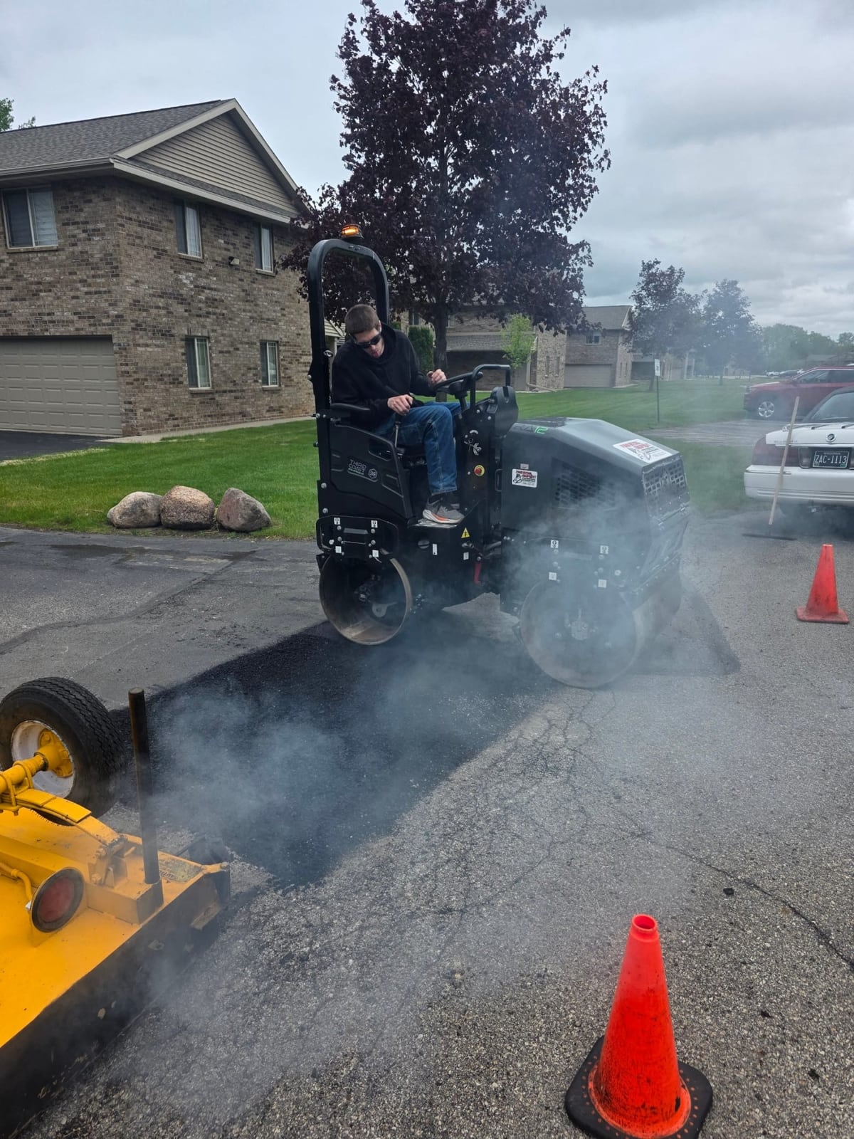 a crew member running asphalt equipment with steam rising on a residential job by Draki Enterprises in Wisconsin