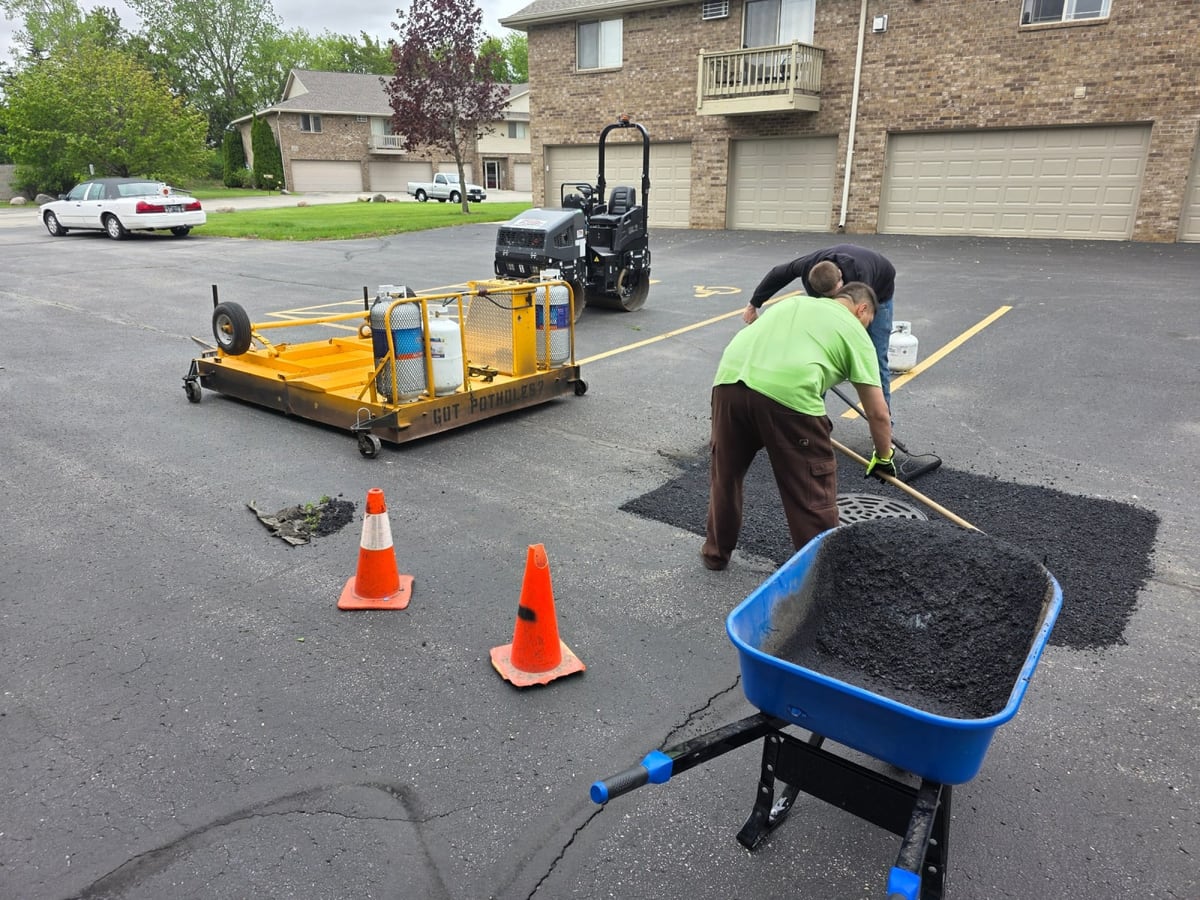 the Draki crew spreading and screeding fresh asphalt to patch a lot, cones set out by Draki Enterprises in Wisconsin