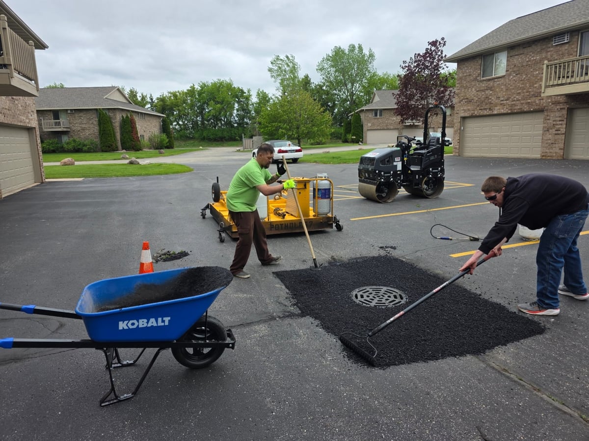 a crew member wheeling and raking fresh asphalt into a repair on a residential drive by Draki Enterprises in Wisconsin