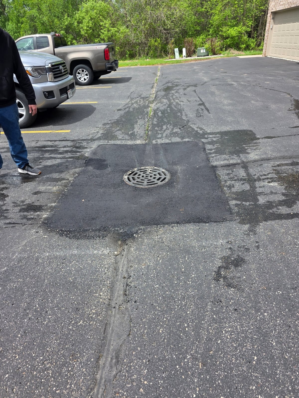 a worn, cracked parking lot around a storm drain before crack sealing and patching by Draki Enterprises in Wisconsin