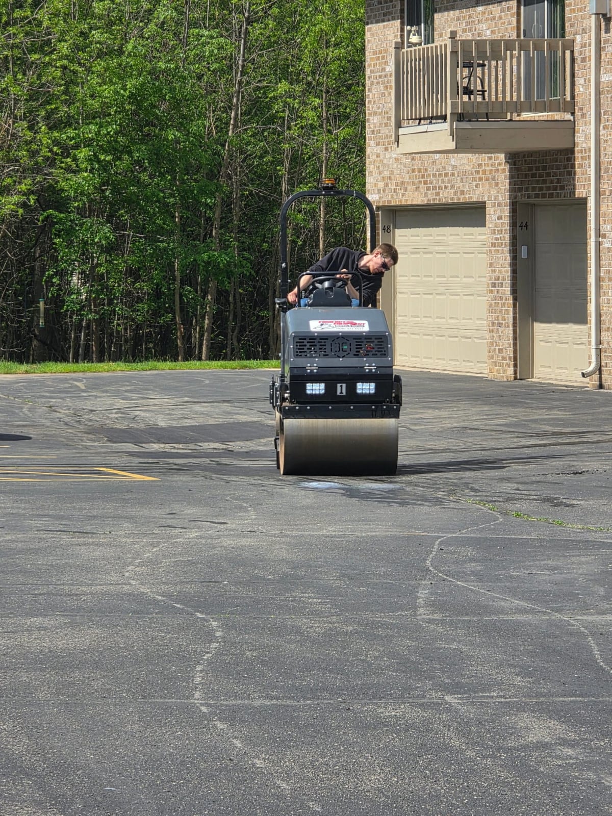 an asphalt roller compacting a fresh repair near a residential garage by Draki Enterprises in Wisconsin