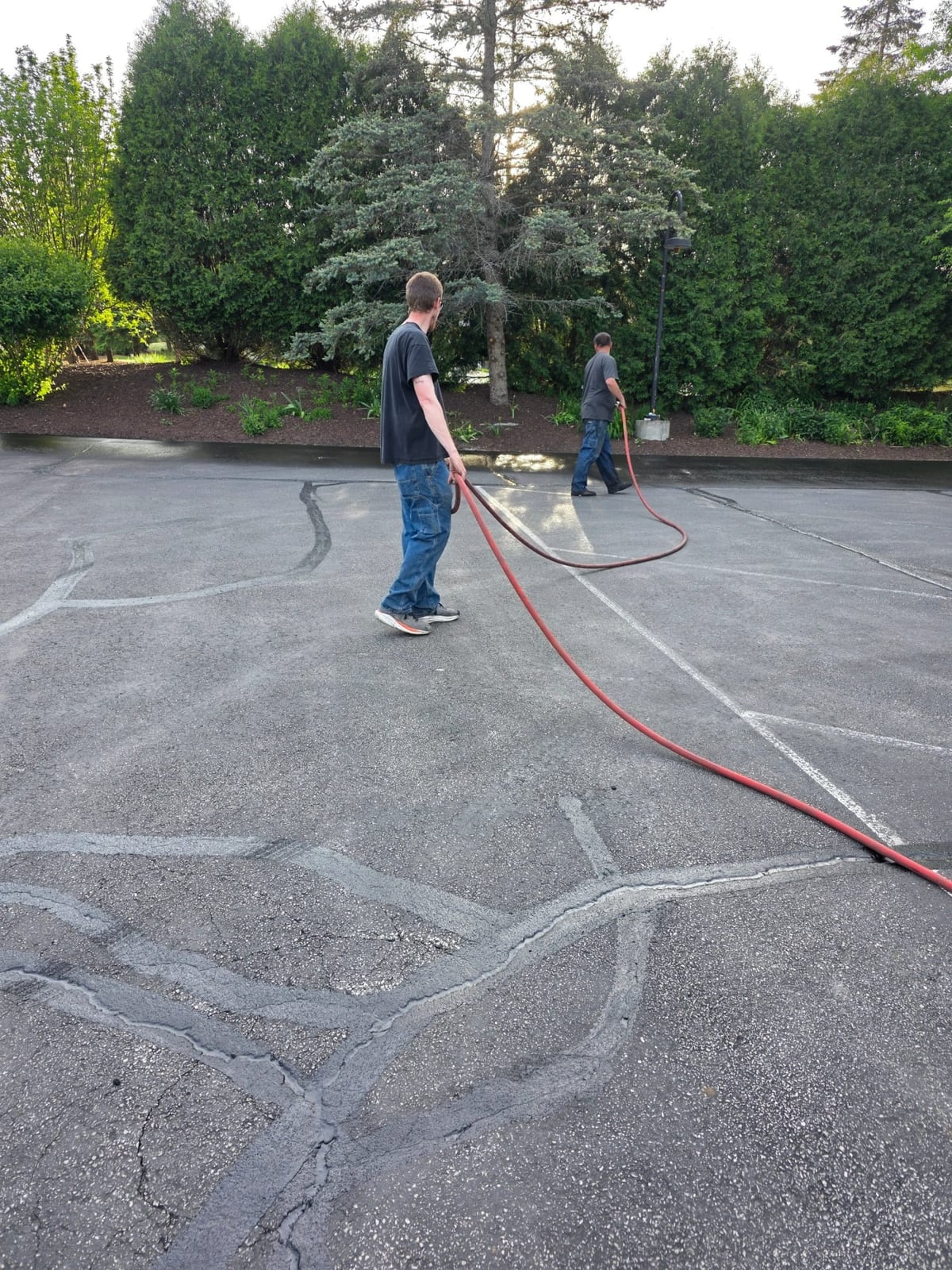 a worker prepping and cleaning an asphalt lot with a hose before sealcoating by Draki Enterprises in Wisconsin