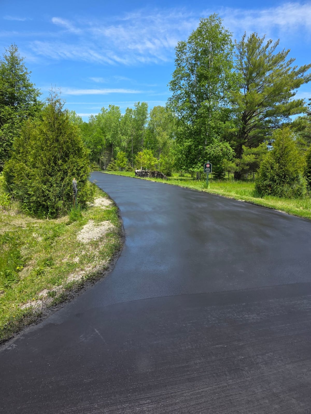 a freshly sealcoated black road curving through trees by Draki Enterprises in Wisconsin