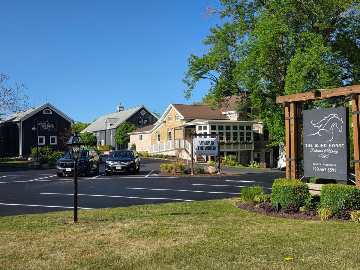 a commercial plaza with parked cars, a monument sign and a sealed, striped lot by Draki Enterprises in Wisconsin