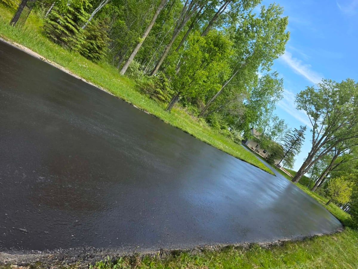 a wide asphalt drive freshly sealcoated to a wet, deep black finish by Draki Enterprises in Wisconsin