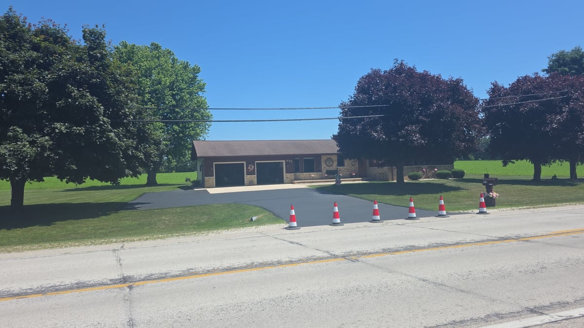 a roadway lined with cones set for striping, a building behind on a clear day by Draki Enterprises in Wisconsin