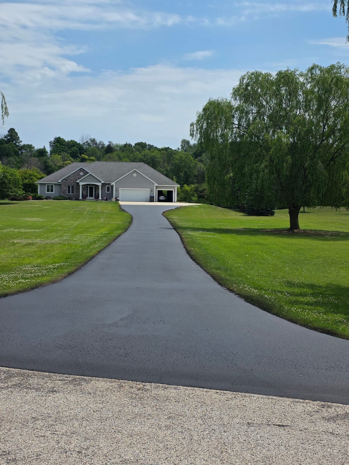 a residential home with a long driveway freshly sealed to a deep black by Draki Enterprises in Wisconsin