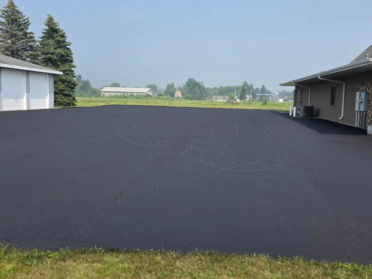 a freshly sealcoated black lot with a garage in the background by Draki Enterprises in Wisconsin